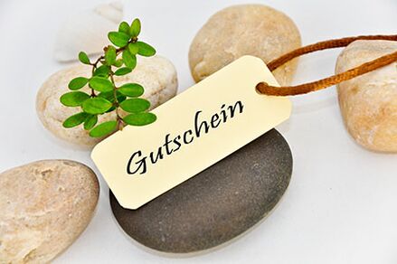 Gutschein Das Bild zeigt fünf größere Kieselsteine, auf denen ein Schild und ein kleiner grüner Zweig liegen. Auf dem Schild steht Gutschein