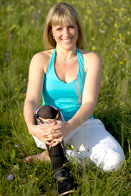 Die Yoga-Lehrerin sitzt entspannt auf einer Wiese und lächelt in die Kamera